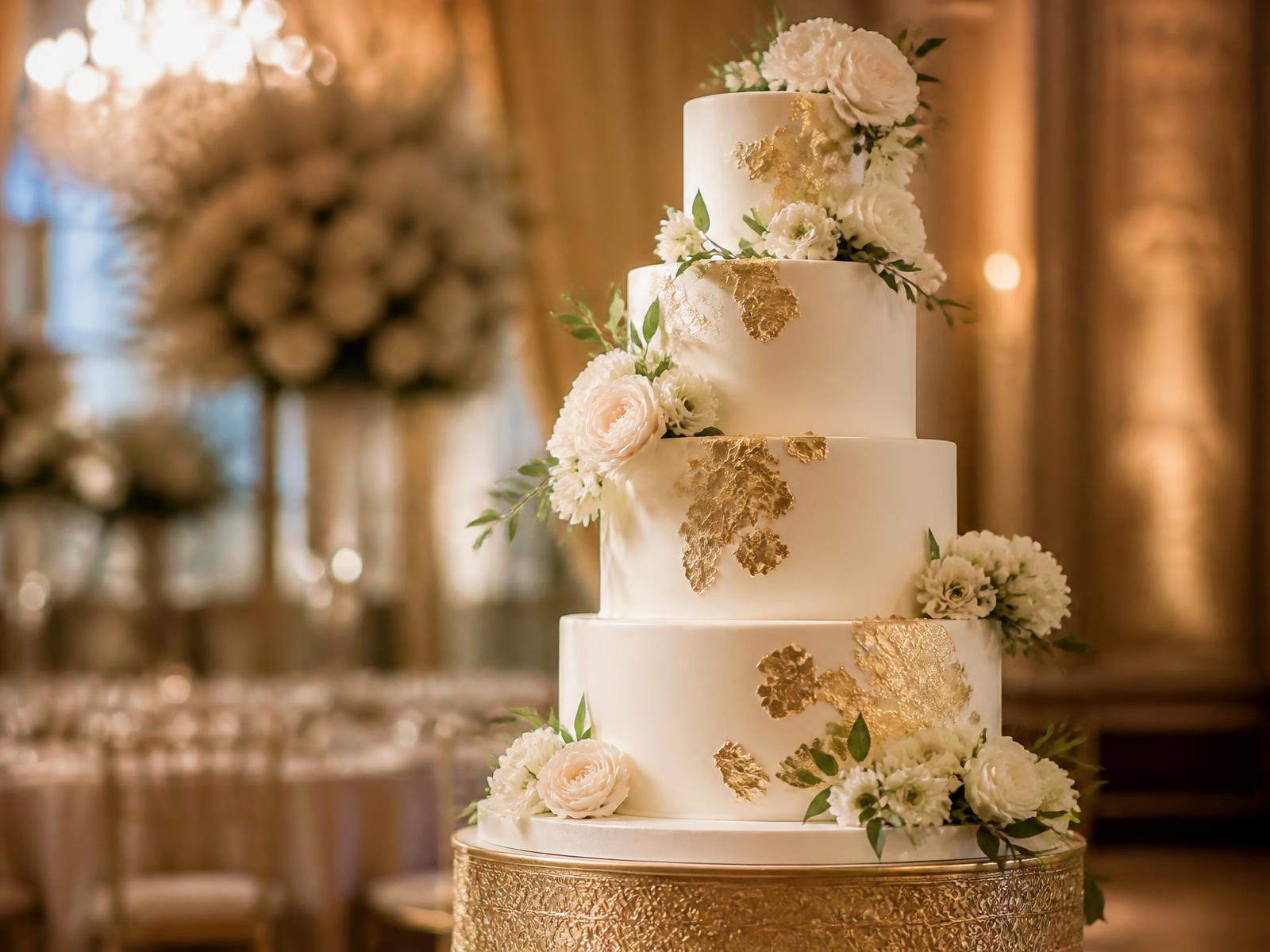 Bolo de casamento de quatro andares com folhas de ouro e flores brancas